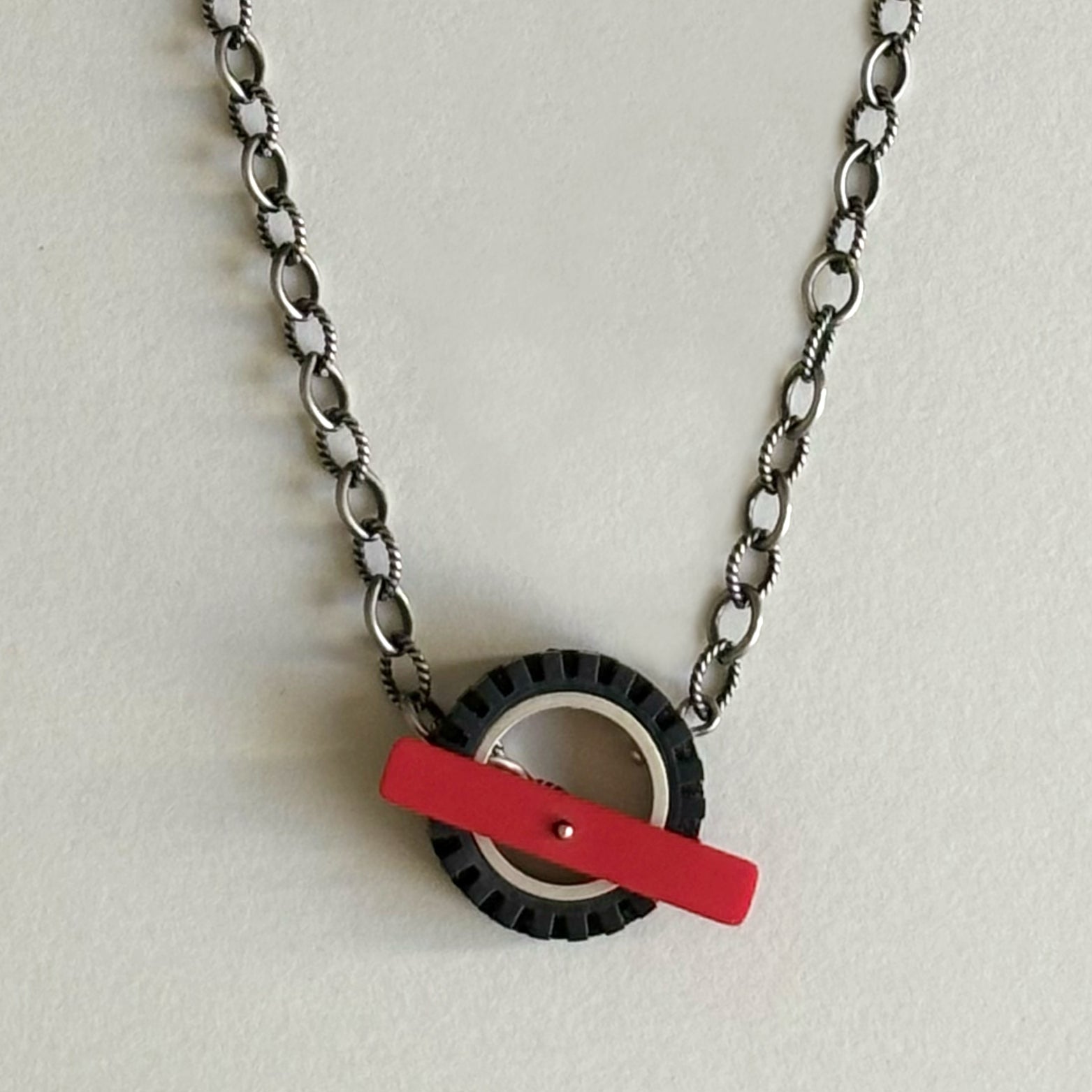 Chunky silver chain with dark finish, with a black LEGO tire on chain with a red recycled LEGO as the toggle clasp in the middle of the LEGO tire
