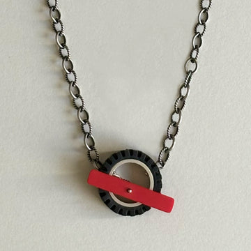 Chunky silver chain with dark finish, with a black LEGO tire on chain with a red recycled LEGO as the toggle clasp in the middle of the LEGO tire
