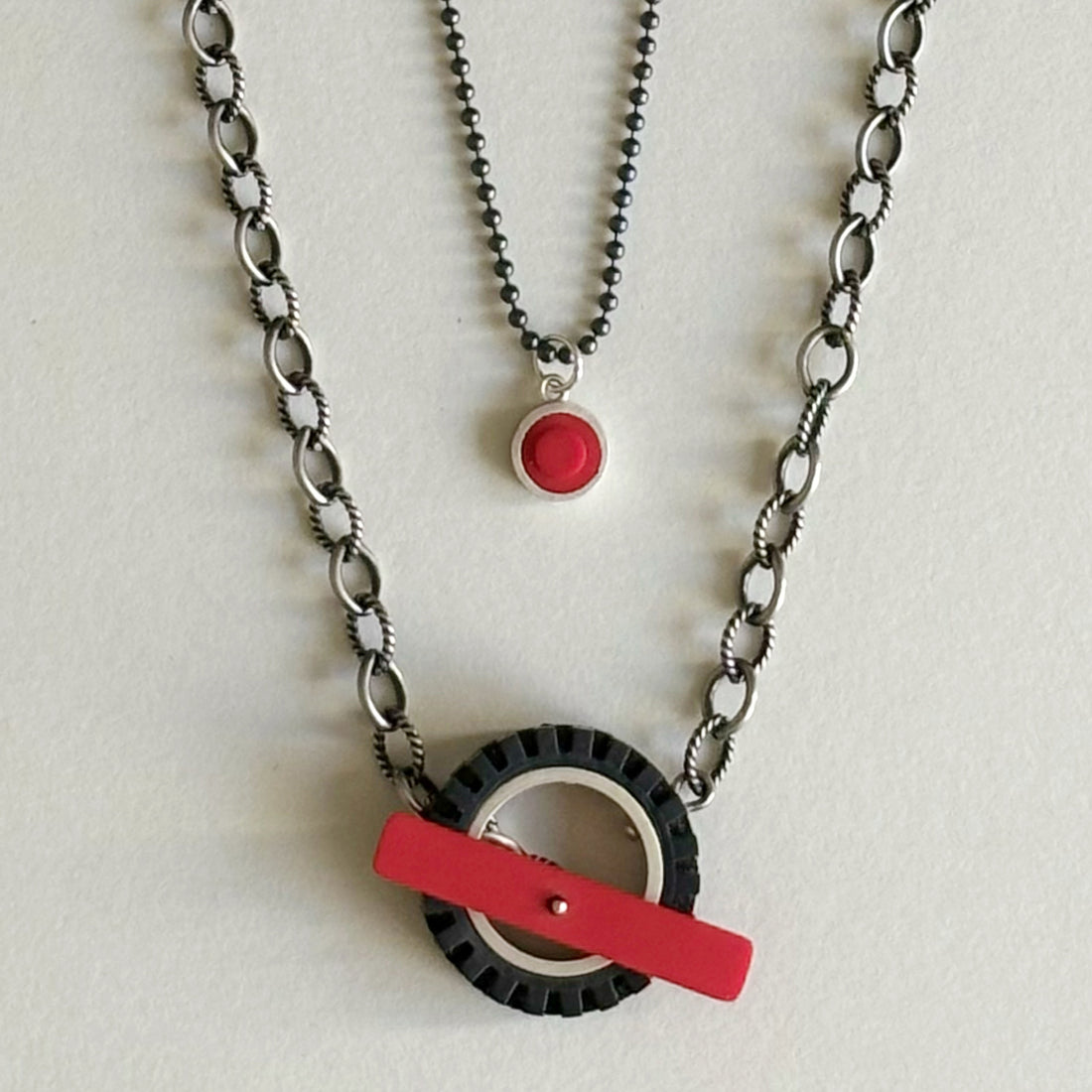 Chunky silver chain with dark finish, with a black LEGO tire on chain with a red recycled LEGO as the toggle clasp in the middle of the LEGO tire