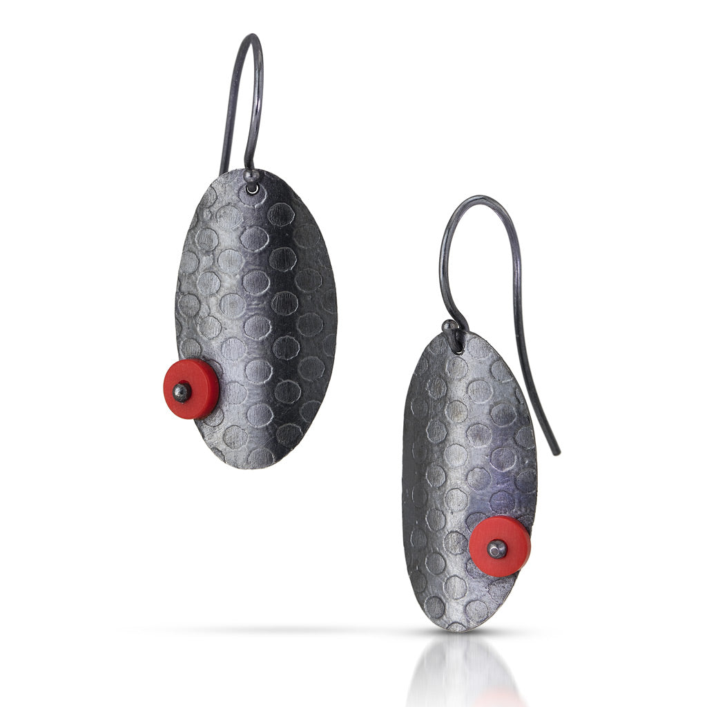 2 dark toned oval shaped earrings that have a round dot pattern embossed and a tiny red dot on opposite sides of each earring. They are displayed off set each other 
