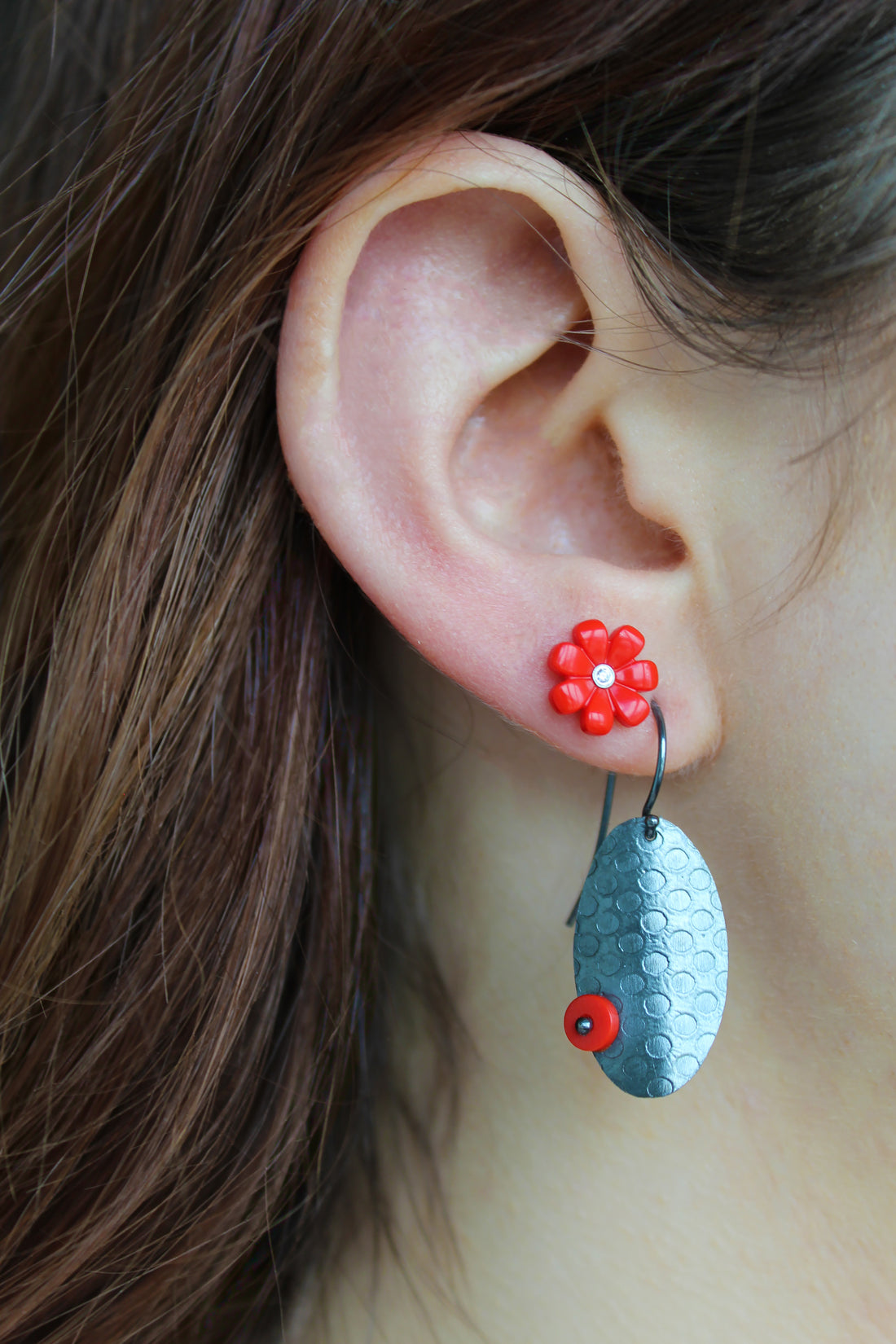 2 dark toned oval shaped earrings that have a round dot pattern embossed and a tiny red dot on opposite sides of each earring. They are displayed off set each other 
